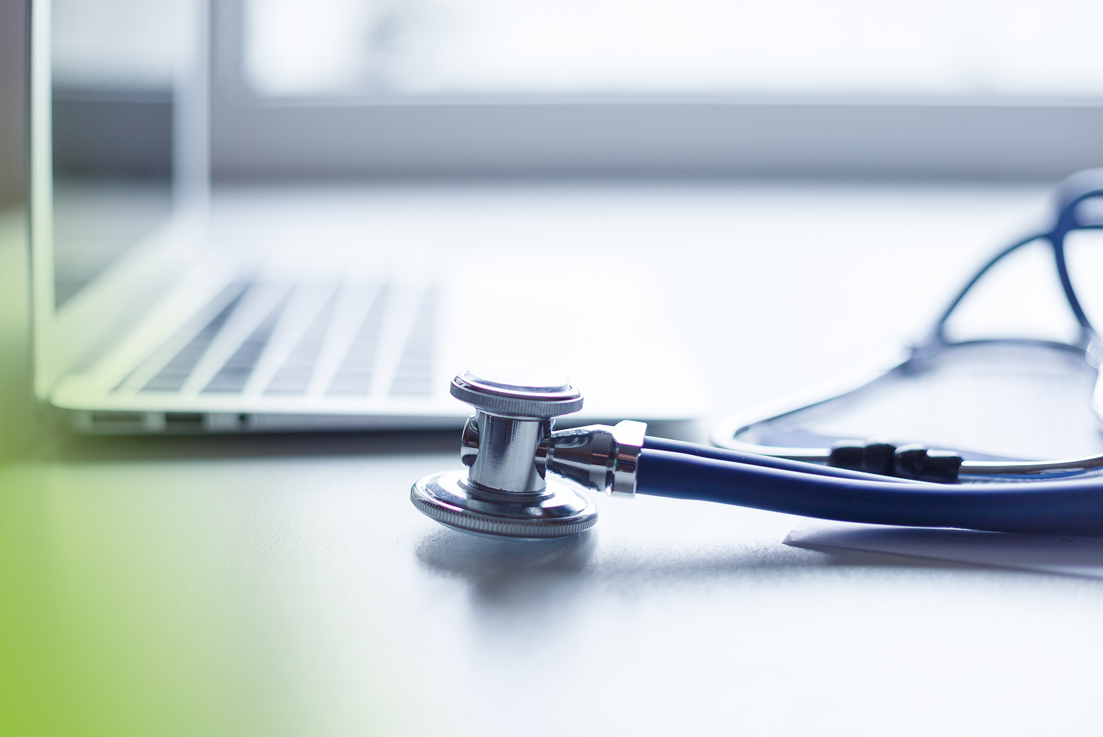 Stethoscope and laptop on doctor working desk with blurred focus for background, business and health care concept